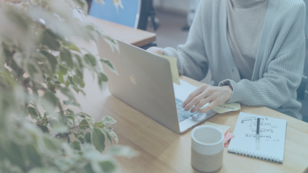 Woman on computer typing with a cup of coffee and a notepad